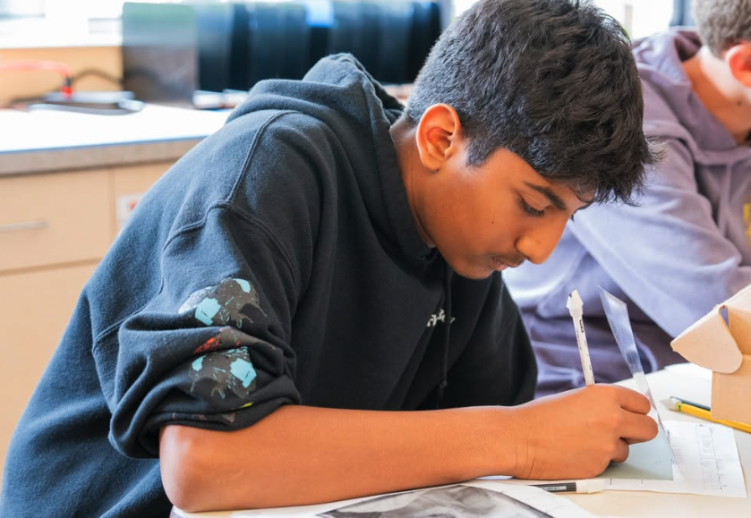 A person sits at a desk drawing on a piece of paper with a pen.