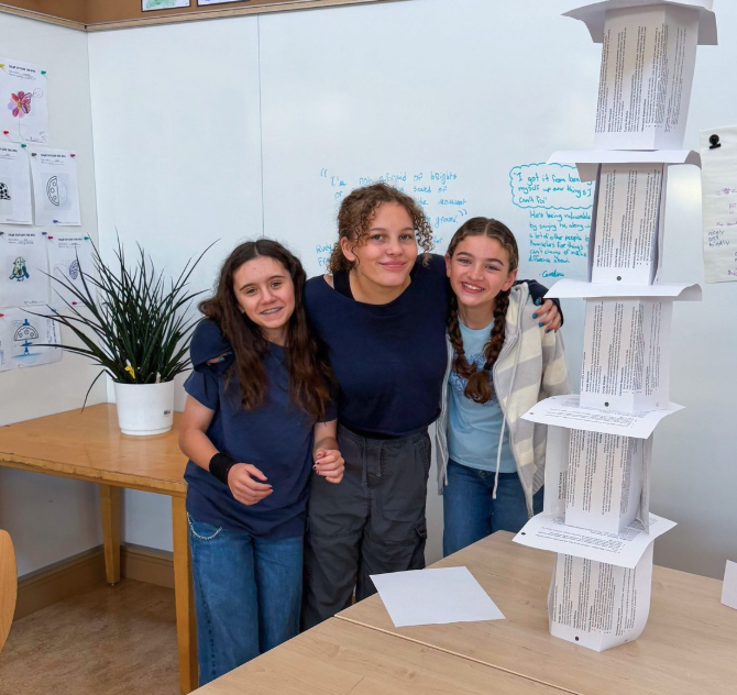 Three people smiling with their arms around each other next to a tall tower made of paper.